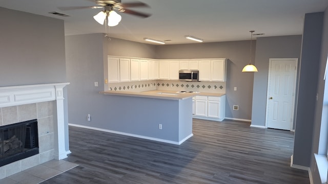 kitchen featuring a tile fireplace, tasteful backsplash, white cabinets, hanging light fixtures, and dark wood-type flooring