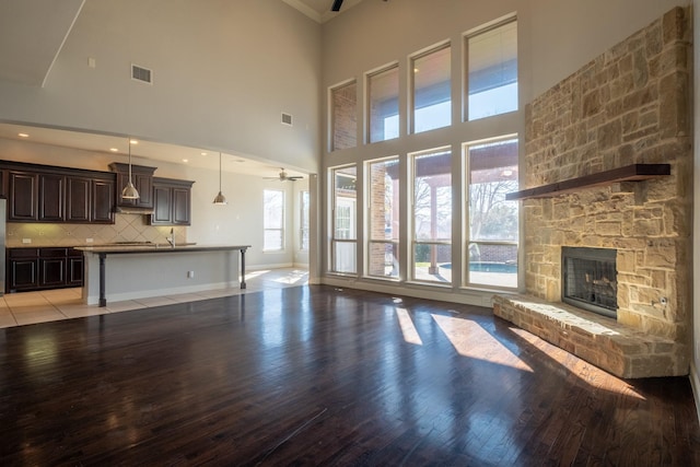 unfurnished living room featuring ceiling fan, a stone fireplace, light hardwood / wood-style flooring, and a high ceiling