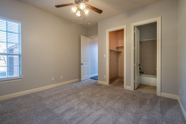 unfurnished bedroom with ensuite bathroom, a spacious closet, light colored carpet, and ceiling fan