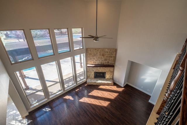 living room with ceiling fan, a towering ceiling, a stone fireplace, and dark wood-type flooring