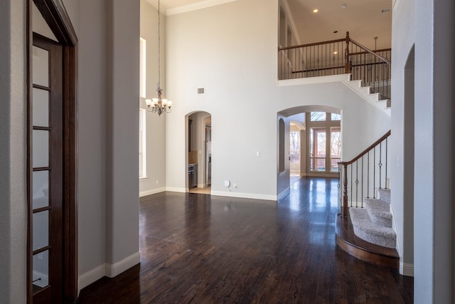 foyer with ornamental molding, a towering ceiling, dark wood-type flooring, and a chandelier