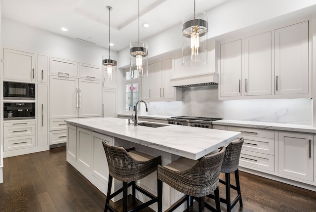 kitchen with sink, white cabinetry, decorative light fixtures, black microwave, and a center island with sink