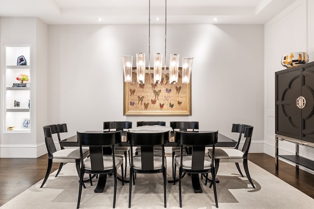 dining area with an inviting chandelier, built in shelves, hardwood / wood-style floors, and a raised ceiling