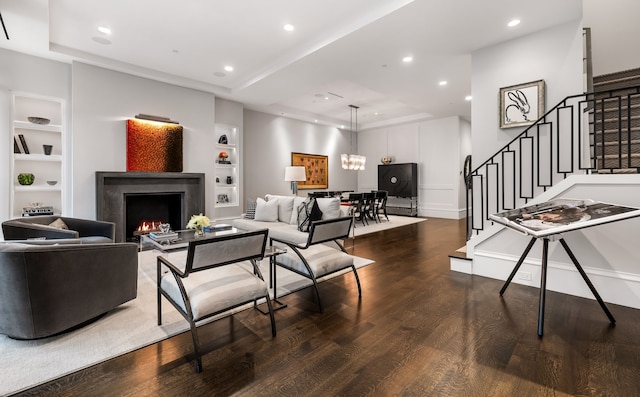 living room with a raised ceiling, dark wood-type flooring, and built in shelves