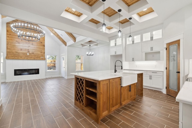 kitchen with sink, hanging light fixtures, beam ceiling, an island with sink, and white cabinets