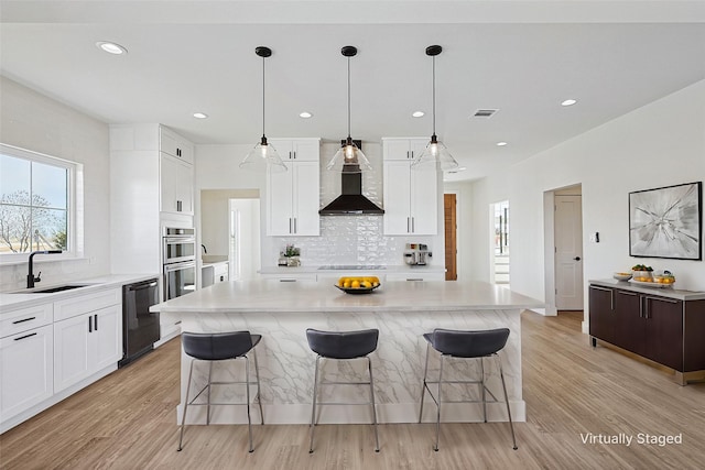 kitchen with a kitchen island, sink, white cabinets, black appliances, and wall chimney range hood