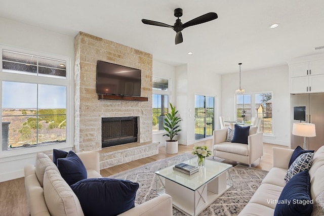 living room with ceiling fan, a healthy amount of sunlight, a stone fireplace, and light hardwood / wood-style flooring