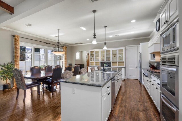 kitchen featuring a kitchen island with sink, tasteful backsplash, stainless steel appliances, and dark stone counters