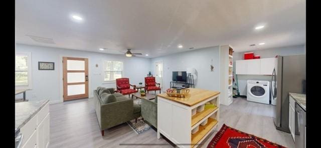 living room featuring ceiling fan, washer / dryer, and light wood-type flooring