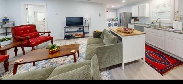 living room featuring independent washer and dryer, sink, and light hardwood / wood-style flooring