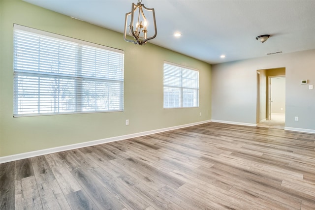 spare room with a healthy amount of sunlight, a chandelier, and light hardwood / wood-style flooring