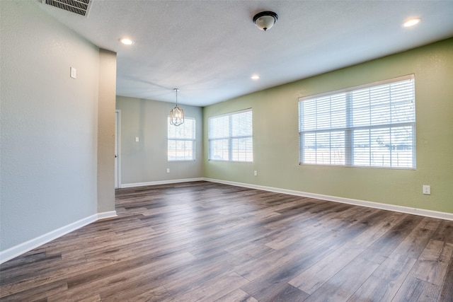 spare room featuring an inviting chandelier, dark hardwood / wood-style floors, and a wealth of natural light