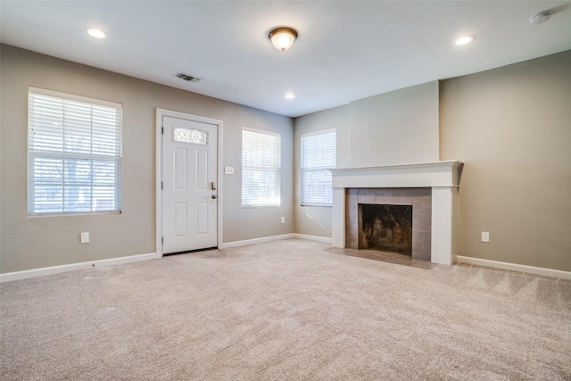 unfurnished living room featuring light colored carpet and a tiled fireplace