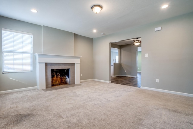 unfurnished living room featuring a tiled fireplace, carpet, and ceiling fan