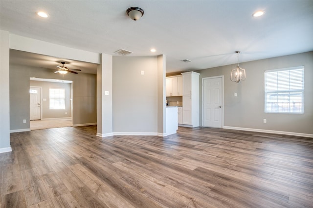 unfurnished living room with ceiling fan with notable chandelier and light hardwood / wood-style floors