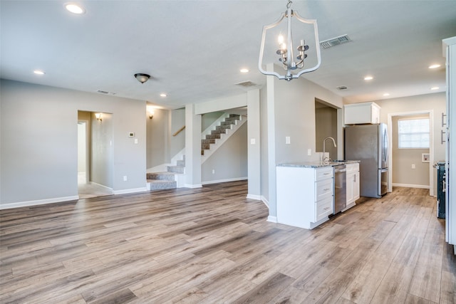 kitchen with white cabinetry, appliances with stainless steel finishes, light stone countertops, and light wood-type flooring