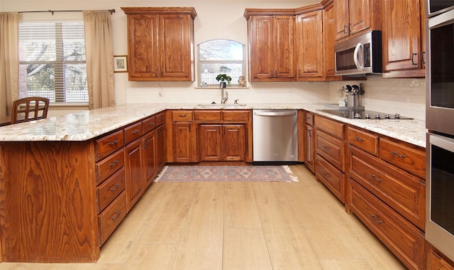 kitchen featuring sink, backsplash, stainless steel appliances, light stone counters, and light wood-type flooring