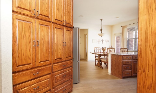 kitchen featuring pendant lighting, light stone counters, stainless steel refrigerator, and light hardwood / wood-style flooring