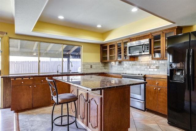 kitchen featuring a raised ceiling, appliances with stainless steel finishes, a center island, and a kitchen bar