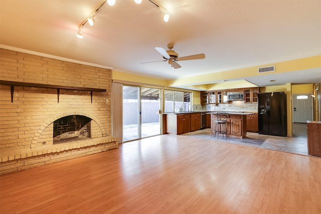 kitchen with appliances with stainless steel finishes, a kitchen bar, decorative backsplash, a brick fireplace, and light hardwood / wood-style flooring