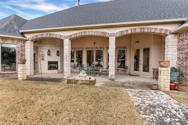 back of house featuring french doors, an outdoor fireplace, a yard, and a patio area