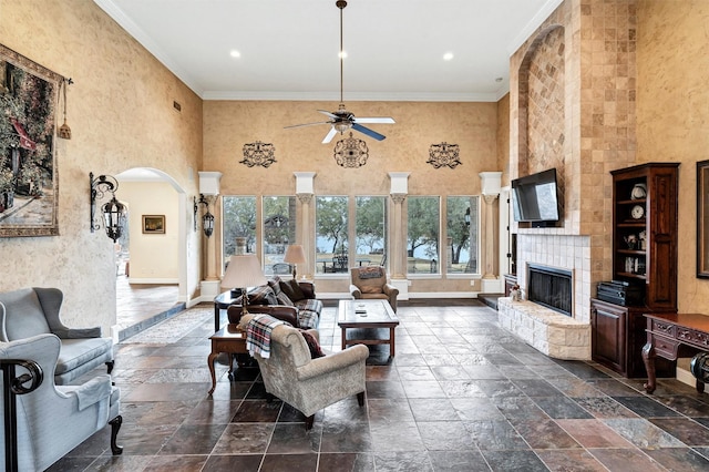 living room featuring a tiled fireplace, ornamental molding, ceiling fan, and a high ceiling