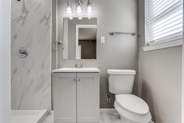 bathroom with a tile shower, vanity, and toilet