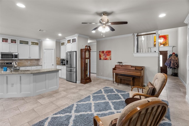 kitchen with appliances with stainless steel finishes, ornamental molding, light stone countertops, white cabinets, and decorative backsplash