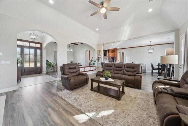 living room featuring arched walkways, baseboards, ceiling fan with notable chandelier, and wood finished floors