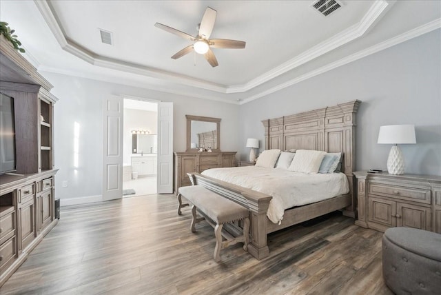 bedroom with ceiling fan, connected bathroom, a tray ceiling, and dark hardwood / wood-style flooring