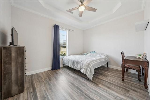 bedroom featuring hardwood / wood-style flooring, ceiling fan, ornamental molding, and a tray ceiling