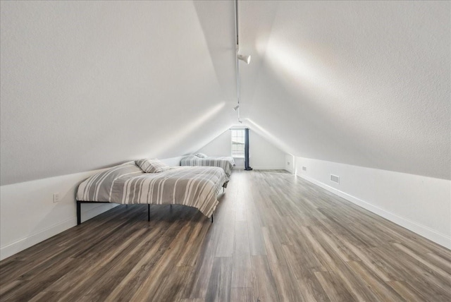 bedroom featuring rail lighting, lofted ceiling, dark hardwood / wood-style floors, and a textured ceiling