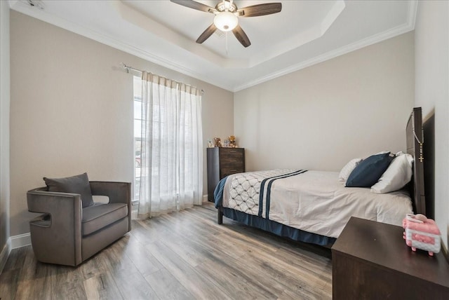 bedroom featuring a ceiling fan, wood finished floors, a raised ceiling, baseboards, and ornamental molding