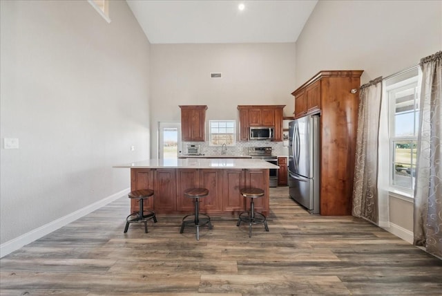 kitchen with a kitchen island, appliances with stainless steel finishes, a breakfast bar, high vaulted ceiling, and dark wood-type flooring