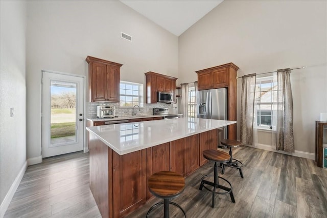 kitchen with appliances with stainless steel finishes, high vaulted ceiling, a kitchen bar, a center island, and dark wood-type flooring