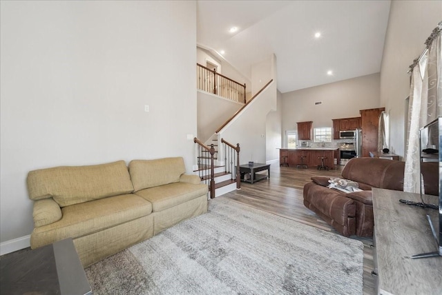 living area featuring baseboards, wood finished floors, high vaulted ceiling, and stairway