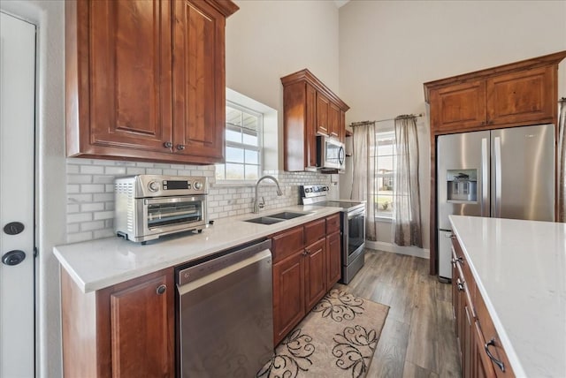 kitchen featuring sink, wood-type flooring, stainless steel appliances, light stone countertops, and backsplash