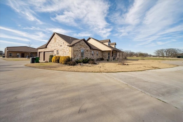 view of side of property featuring an attached garage, stone siding, and concrete driveway