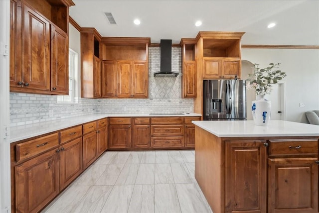 kitchen with wall chimney range hood, open shelves, stainless steel fridge with ice dispenser, brown cabinetry, and visible vents