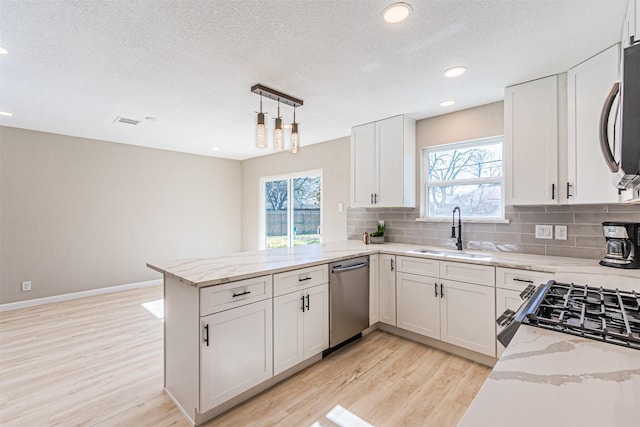 kitchen with sink, appliances with stainless steel finishes, tasteful backsplash, white cabinets, and kitchen peninsula