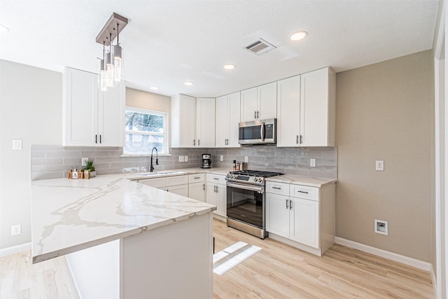 kitchen featuring white cabinetry, sink, decorative light fixtures, and appliances with stainless steel finishes