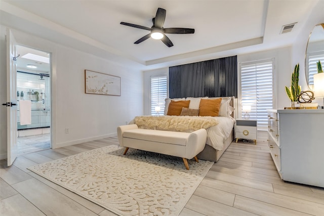 bedroom featuring multiple windows, a tray ceiling, and light wood-type flooring