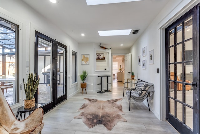 hall featuring french doors, a skylight, and light hardwood / wood-style flooring