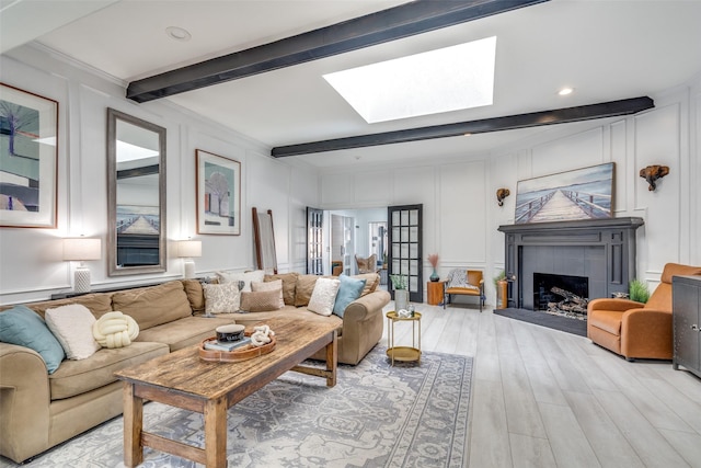 living room featuring a skylight, a tile fireplace, light hardwood / wood-style floors, and beamed ceiling