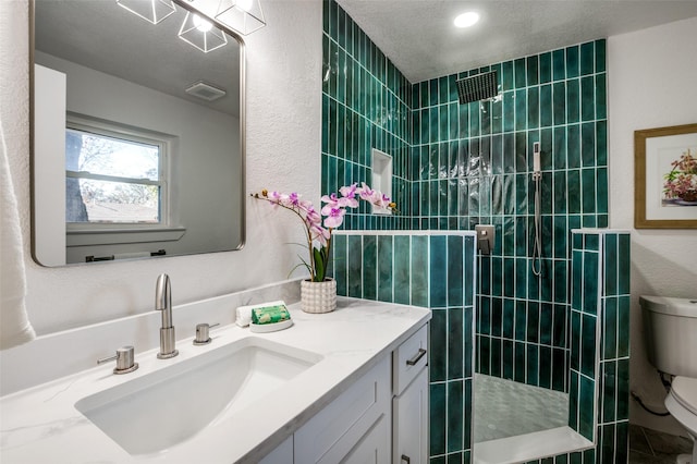 bathroom with vanity, a textured ceiling, toilet, and a tile shower