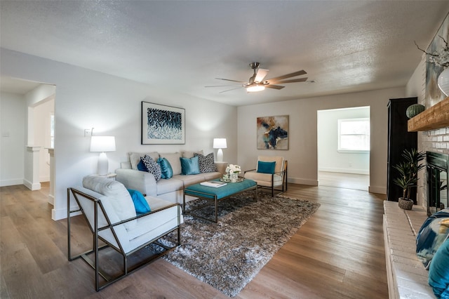 living room featuring ceiling fan, a brick fireplace, hardwood / wood-style floors, and a textured ceiling