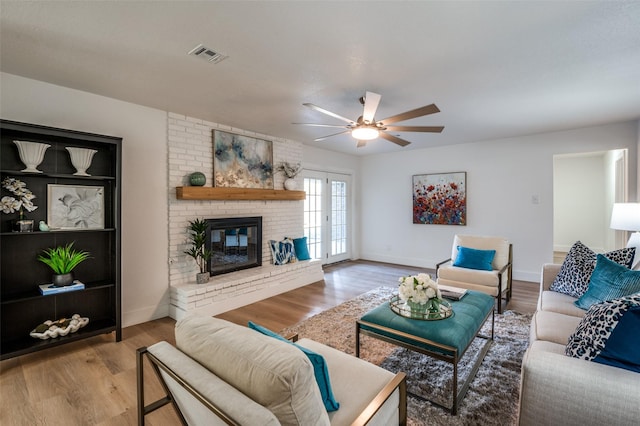 living room with ceiling fan, a brick fireplace, light hardwood / wood-style floors, and french doors