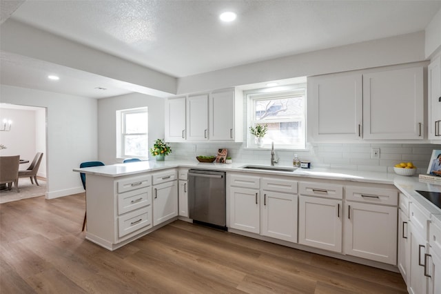 kitchen featuring sink, tasteful backsplash, white cabinets, stainless steel dishwasher, and kitchen peninsula