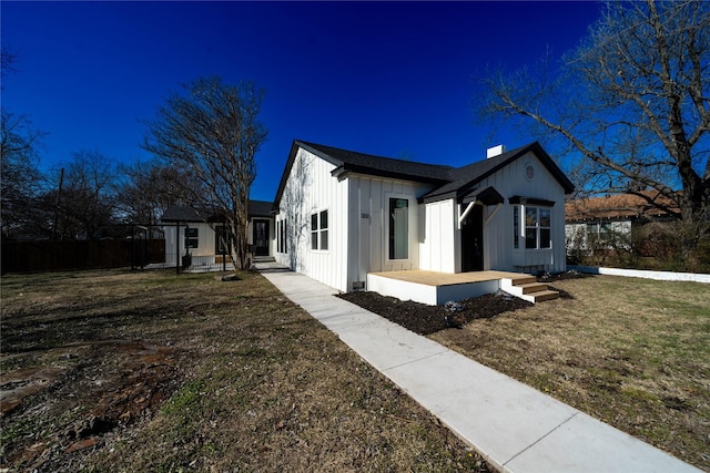 view of side of home featuring board and batten siding, a yard, a chimney, and fence