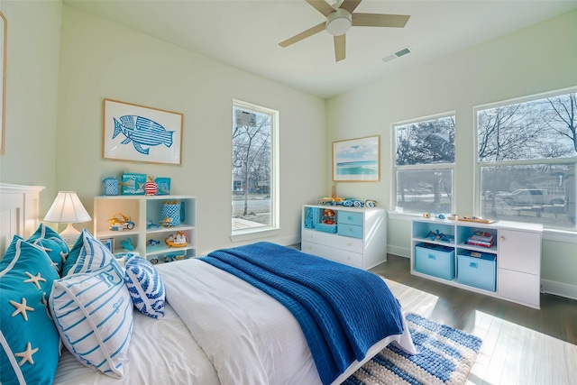 bedroom with a ceiling fan, visible vents, baseboards, and wood finished floors